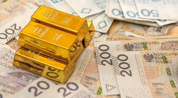 Sztabki złota na stosie polskich banknotów. Rozważasz sprzedaż złota i zastanawiasz się nad podatkiem?
