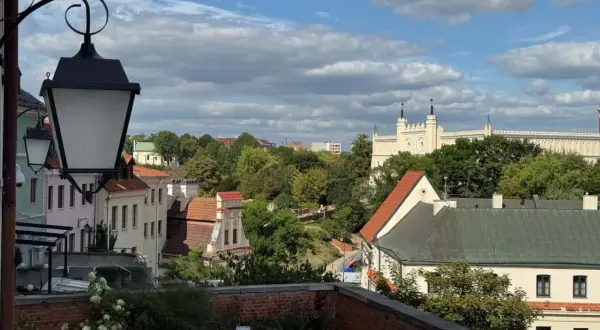 Widok na Lublin na weekend. Zabytkowe kamienice, zieleń i biały zamek na wzgórzu pod błękitnym niebem.