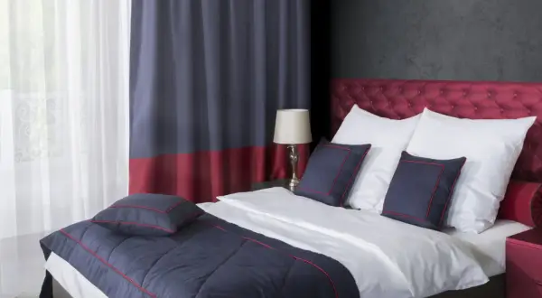 Eleganckie łóżko z pikowanym zagłówkiem, białą pościelą i granatowymi poduszkami. Pokazuje, jak pościelić łóżko w stylu hotelowym.