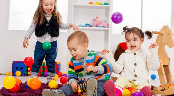 Radosne zabawy w przedszkolu! Dzieci rzucają kolorowymi piłeczkami, śmiejąc się wesoło.