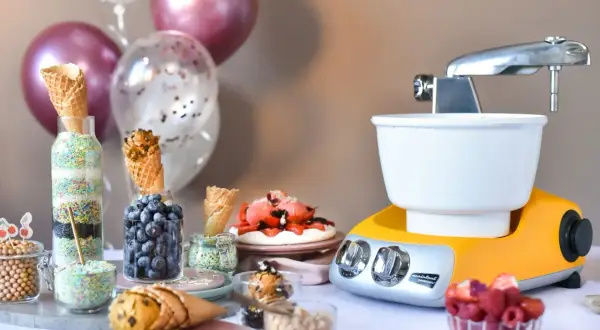 En gul och silverfärgad frozen yoghurt glassmaskin står redo för fest. Strössel, bär och våfflor väntar på att bli till godsaker.