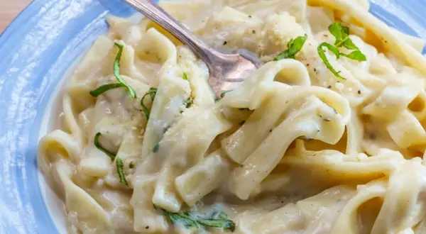 Pyszny makaron z tuńczykiem w sosie śmietanowo-serowym, udekorowany świeżą bazylią i parmezanem.