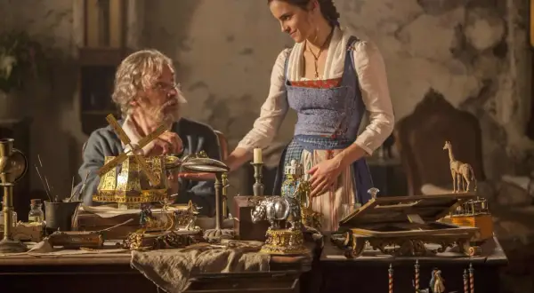 Bella y su padre, Maurice, observan un intrincado molino de viento dorado. La escena evoca la magia de "la bella y la bestia".