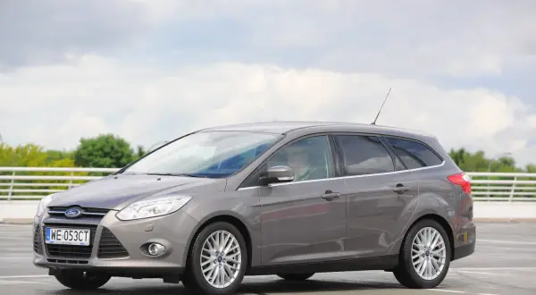 Szary Ford Focus MK3 kombi, z widocznymi reflektorami i felgami. Idealny do miasta i na wakacje, z pewnością z dobrymi żarówkami.