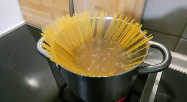 Długie spaghettoni gotują się w garnku na kuchence.
