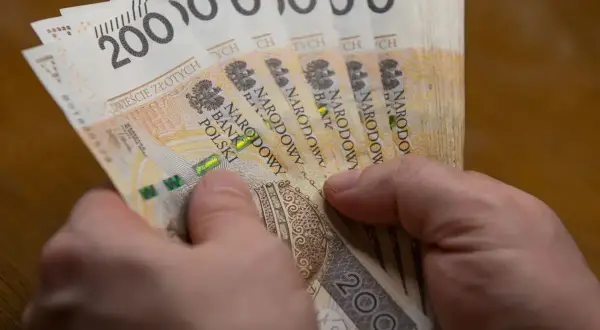 Dłonie trzymają plik banknotów po 200 zł. To może być wypłata, która wynosi 5000 brutto.