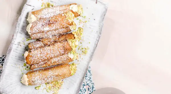 En bricka med flera italienska bakelser, cannolis, pudrade med florsocker och garnerade med hackade pistagenötter.