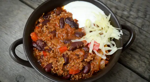 Pyszne chili con carne przepis: sycące danie z mielonym mięsem, fasolą i warzywami, podane z kwaśną śmietaną i startym serem.