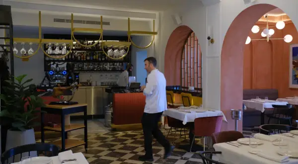 Interior de restaurantes arrabal Zaragoza. Mesas puestas, barra con botellas y un chef camina.