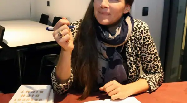 Esther Maria Magnis hält einen Stift und blickt nachdenklich. Auf dem Tisch liegt ihr Buch "Gott braucht dich nicht".