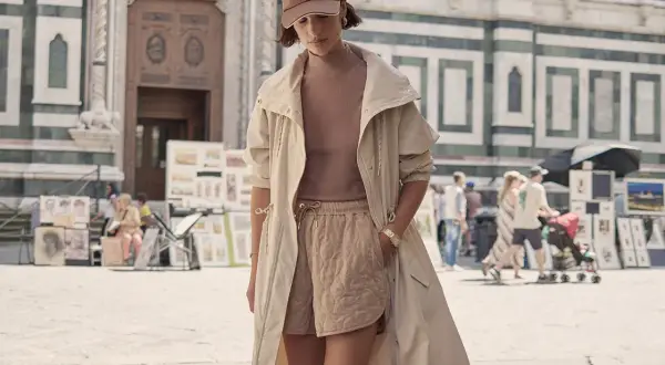 Frau im Athleisure Style mit beiger Jacke und gesteppten Shorts vor einer historischen Fassade.