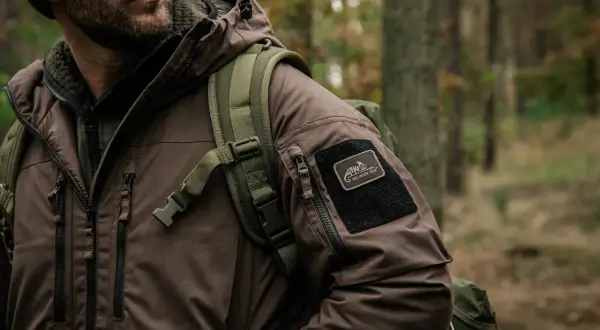 Mężczyzna w brązowej kurtce z naszywką Helikon-Tex, gotowy na przygodę. To dowód, że polskie marki outdoorowe to jakość i styl.