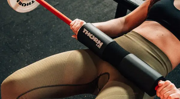 Kobieta wykonuje hip thrust po polsku z gryfem i obciążeniem.