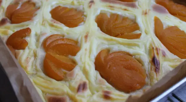 Wilgotne ciasto jogurtowe z budyniem i brzoskwiniami, pieczone w kwadratowej formie.