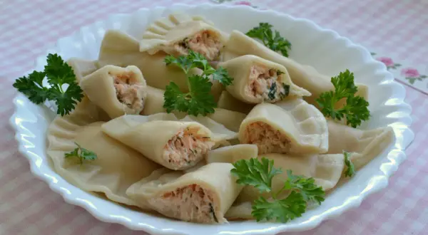 Pyszne pierogi z łososiem, delikatnie ugotowane, podane na białym talerzu z natką pietruszki.