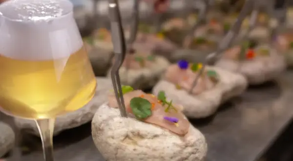 Un bicchiere di birre ale italiane accanto a tartare di pesce su pietre.