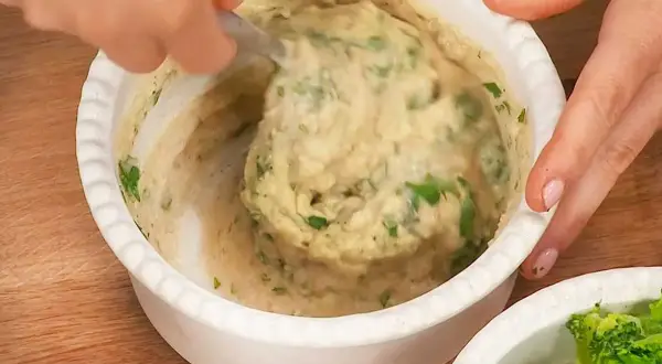 En hand rör i en skål med krämiga refried beans och färska örter.