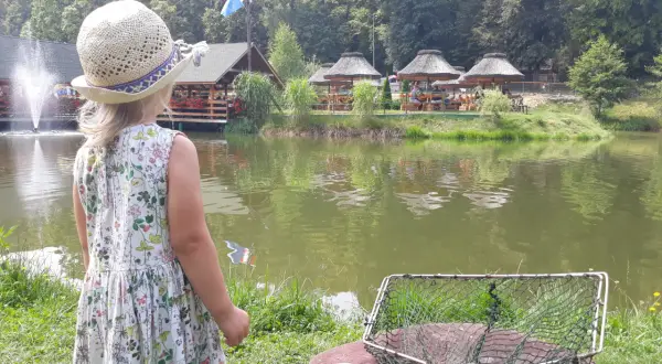 Dziewczynka w słomkowym kapeluszu patrzy na łowisko na wyspie Pokrzywna. Obok niej leży podbierak i kukurydza.