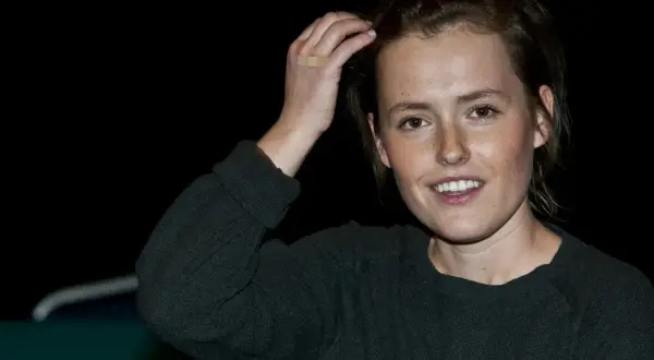 Olga Frycz, młoda kobieta z piegami, uśmiecha się, poprawiając włosy. Na jej dłoni plaster.
