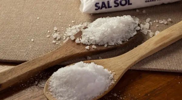 Dos cucharas de madera muestran cómo se obtiene la sal: una con sal marina gruesa y otra con sal fina, junto a un paquete de Sal Sol.