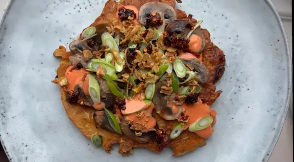 En krispig japansk kålpannkaka toppad med champinjoner, salladslök, krispiga lökar och en krämig sås.
