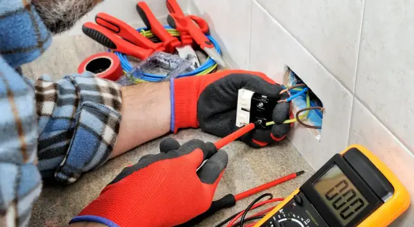 Un électricien utilise des outils pour installer une prise. On voit des fils, un tournevis, un multimètre et d'autres outils pour électricien.