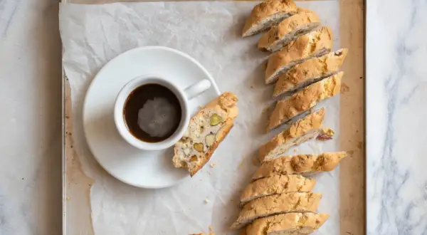 En kopp kaffe bredvid en rad med italiensk mandelskorpa, bakad med nötter och pistagenötter.