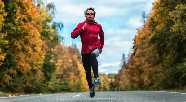 Un homme court sur une route bordée d'arbres aux couleurs d'automne, en plein effort, comme lors d'une séance fractionné.