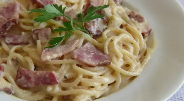 Pyszne spaghetti z boczkiem w kremowym sosie, udekorowane natką pietruszki. Idealne danie dla miłośników włoskiej kuchni.