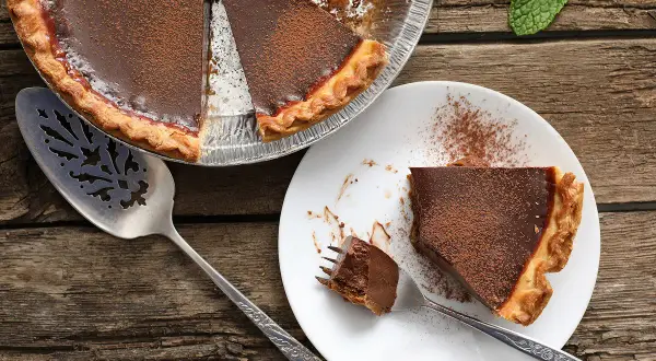 Une délicieuse tarte au chocolat, parfaite pour une recette gourmande. Une part est servie sur une assiette, prête à être dégustée.