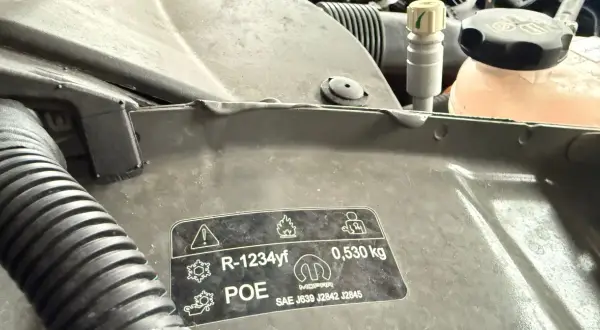 Naklejka z informacją o czynniku klimatyzacji R-1234yf i jego cenie. Wskazuje na ilość 0,530 kg.