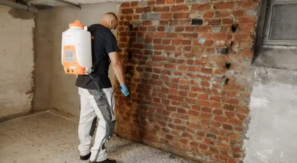 Mann mit Sprühgerät dichtet Ziegelwand im Keller ab.