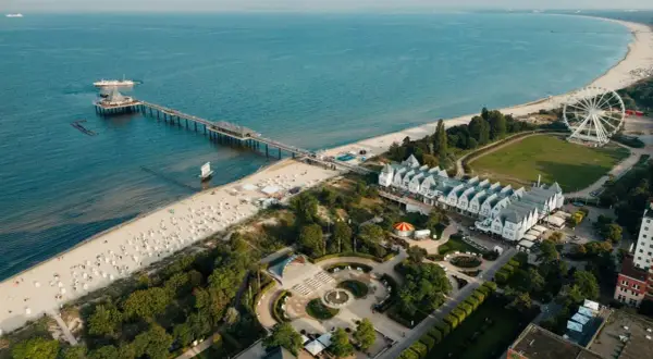Widok na plażę, molo i białe budynki z dachami w szpic na wyspie Uznam. W oddali widać diabelski młyn.