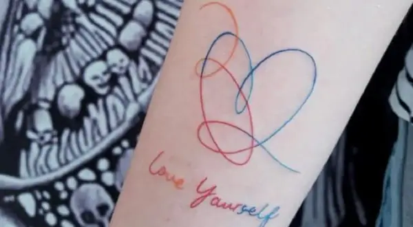 Tatuajes de corazón y "Love Yourself" en el brazo, un símbolo de fortaleza y amor propio.