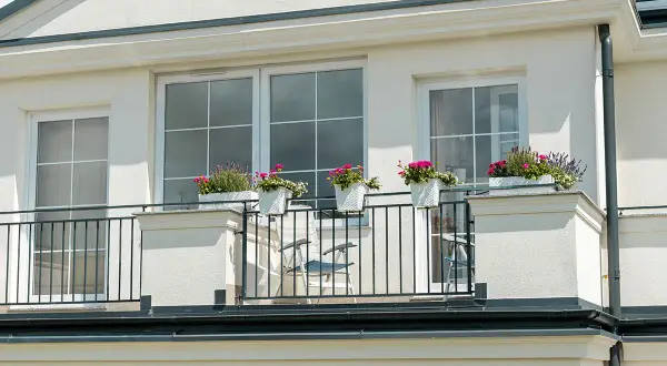 Białe okna pięknie komponują się z jasną, kremową elewacją budynku. Balkon ozdobiony kwiatami dodaje uroku.