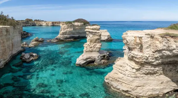 Klippformationer reser sig ur det turkosa vattnet vid Salento, Italien. En kajakpaddlare njuter av den vackra kusten.