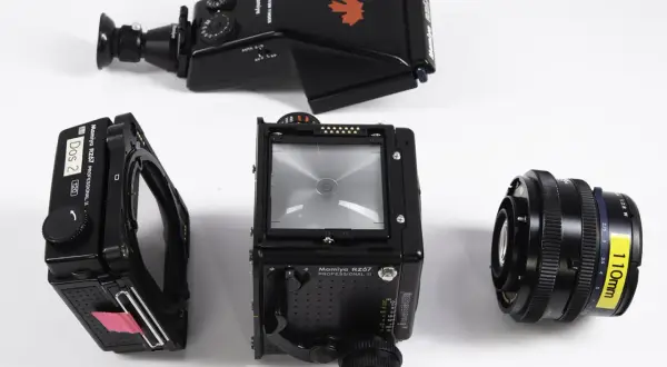 A Mamiya RZ67 camera body, film back, prism finder, and 110mm lens are laid out on a white surface.