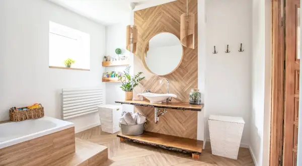 Salle de bain moderne avec sol et murs en bois, baignoire, lavabo et miroir. On peut mettre du parquet dans une salle de bain si le matériau est adapté.