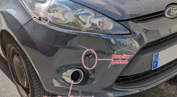 Avant le contrôle technique : feu antibrouillard avant cassé, bouclier perforé et projecteur endommagé sur une voiture grise.