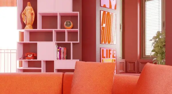 Pomarańczowa kanapa i różowe regały tworzą radosny, **dopamine decor**. Na półce figurka, zegar, telefon i książki. Obok plakaty z napisami.