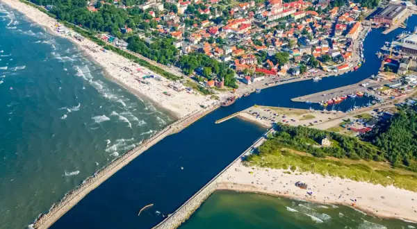Widok z lotu ptaka na miasto i port, gdzie rzeka płynie przez Ustkę. Widać plażę, morze, falochrony i łodzie.