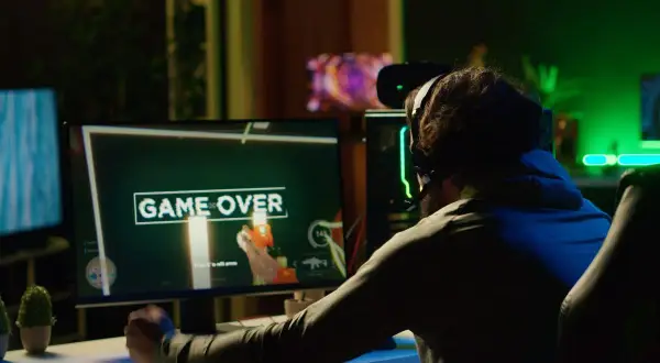 Gracz sfrustrowany przegraną, ekran "GAME OVER". Może to znak, że czas pomyśleć, jak zmniejszyć ping i poprawić swoje wyniki w grach online.