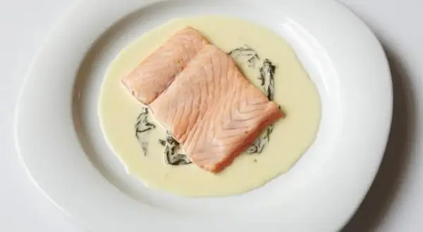 Deux pavés de saumon poêlés, nappés d'une onctueuse sauce oseille, servis sur une assiette blanche.