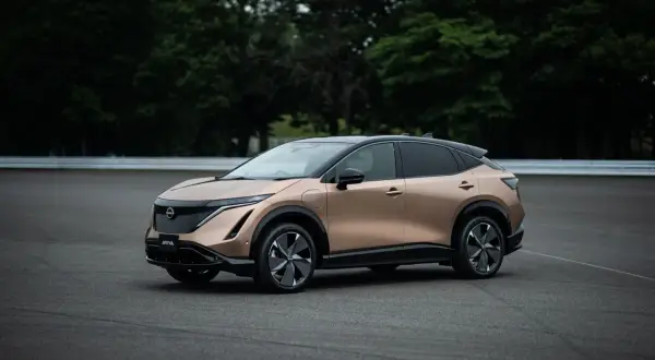 Elegancki, brązowy Nissan Ariya na tle zielonych drzew i asfaltu.