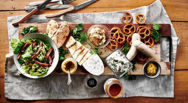 Herzhafte deutsche Gerichte: Wurst, Käse, Brezeln, Salat und Brot auf rustikaler Platte.