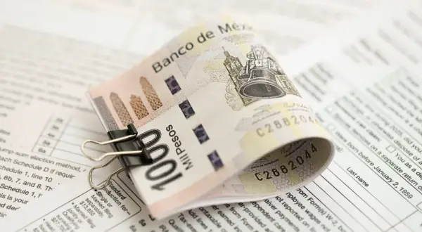 Złożony banknot 100 pesos, przytrzymany spinaczem, leży na dokumentach podatkowych. To pokazuje, co to jest lokata bankowa – sposób na bezpieczne przechowywanie pieniędzy.