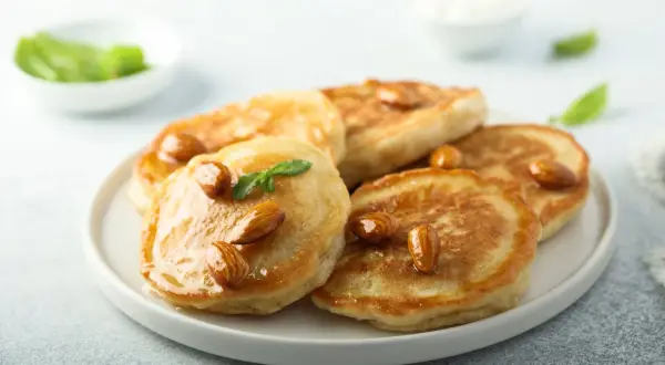 Pancakes con farina di mandorle, guarniti con mandorle intere e sciroppo dorato, su un piatto bianco.