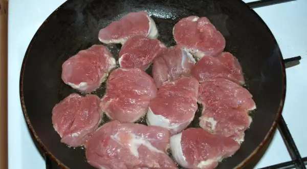 Kawałki polędwiczki wieprzowej smażące się na patelni.
