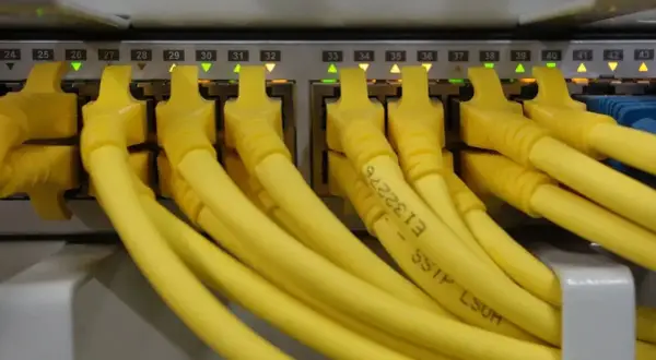 Conectores amarillos de red en un panel, cada uno con una luz verde o naranja encendida. Parece un splitter de red.