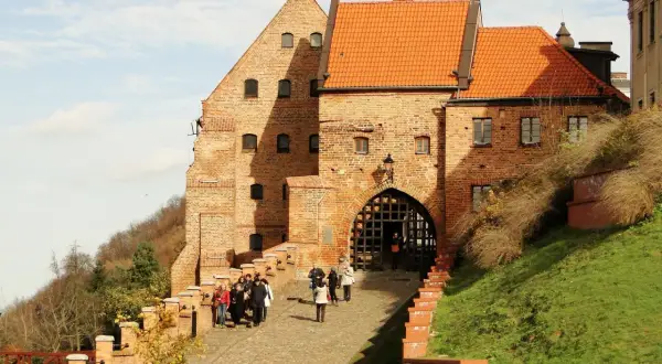 Zamek w Grudziądzu z bramą i grupą turystów na brukowanej ścieżce.